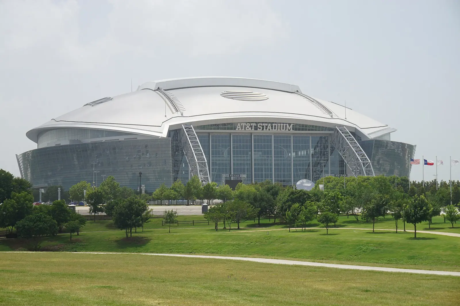 The white-roofed exterior of AT&T Stadium in Arlington, Texas seen across a green park