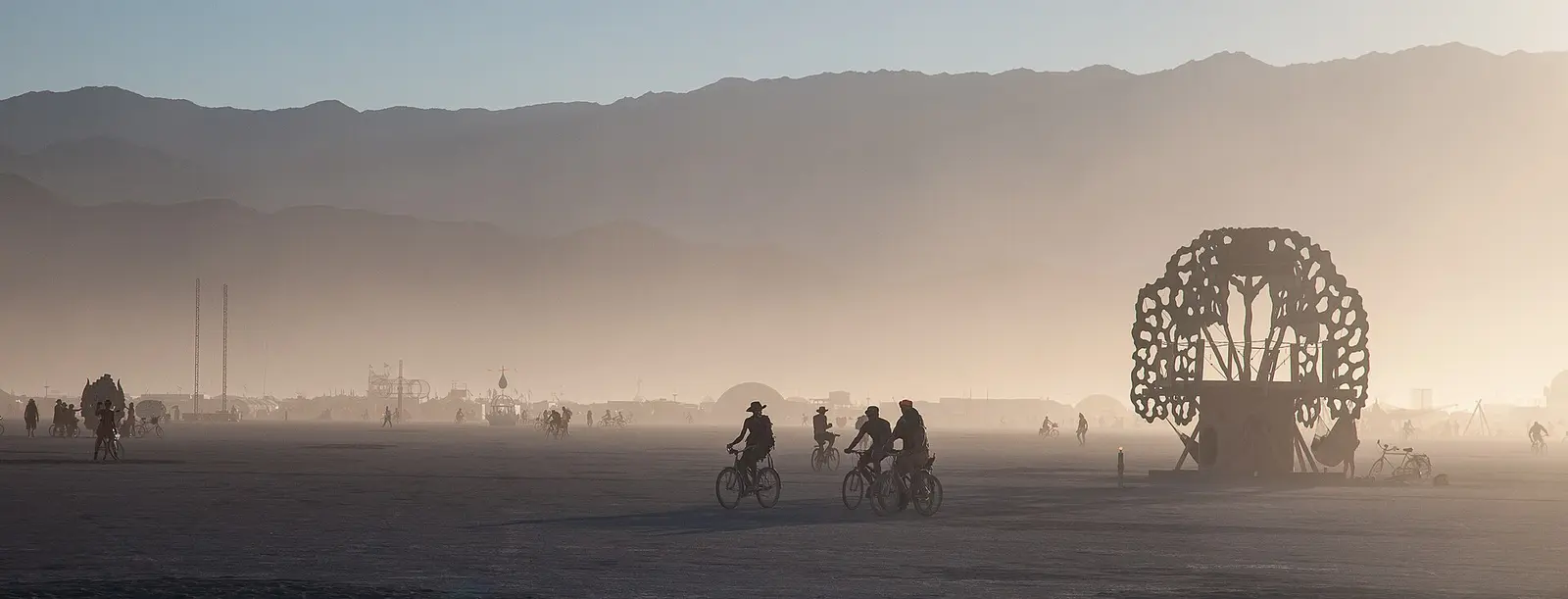Cyclists crossing the dusty playa at Burning Man in 2012 with mountains behind