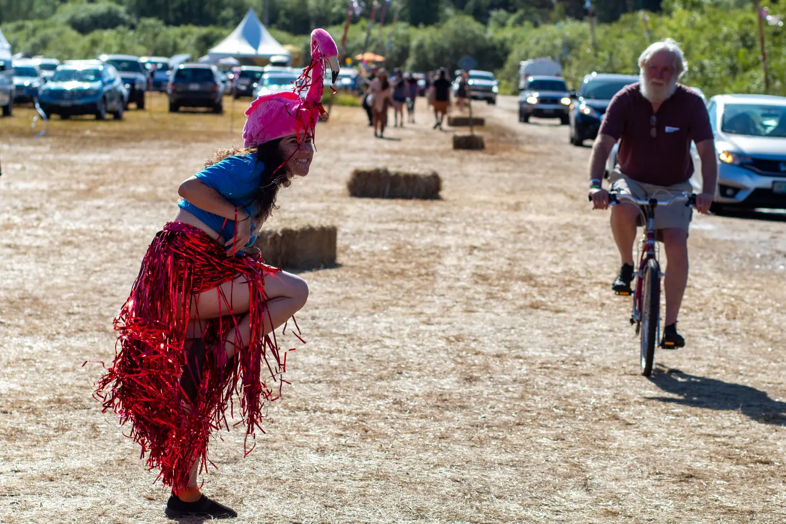 A costumed fairgoer in a red fringed outfit crosses the dirt lot at the 2022 Oregon Country Fair as a cyclist rides past