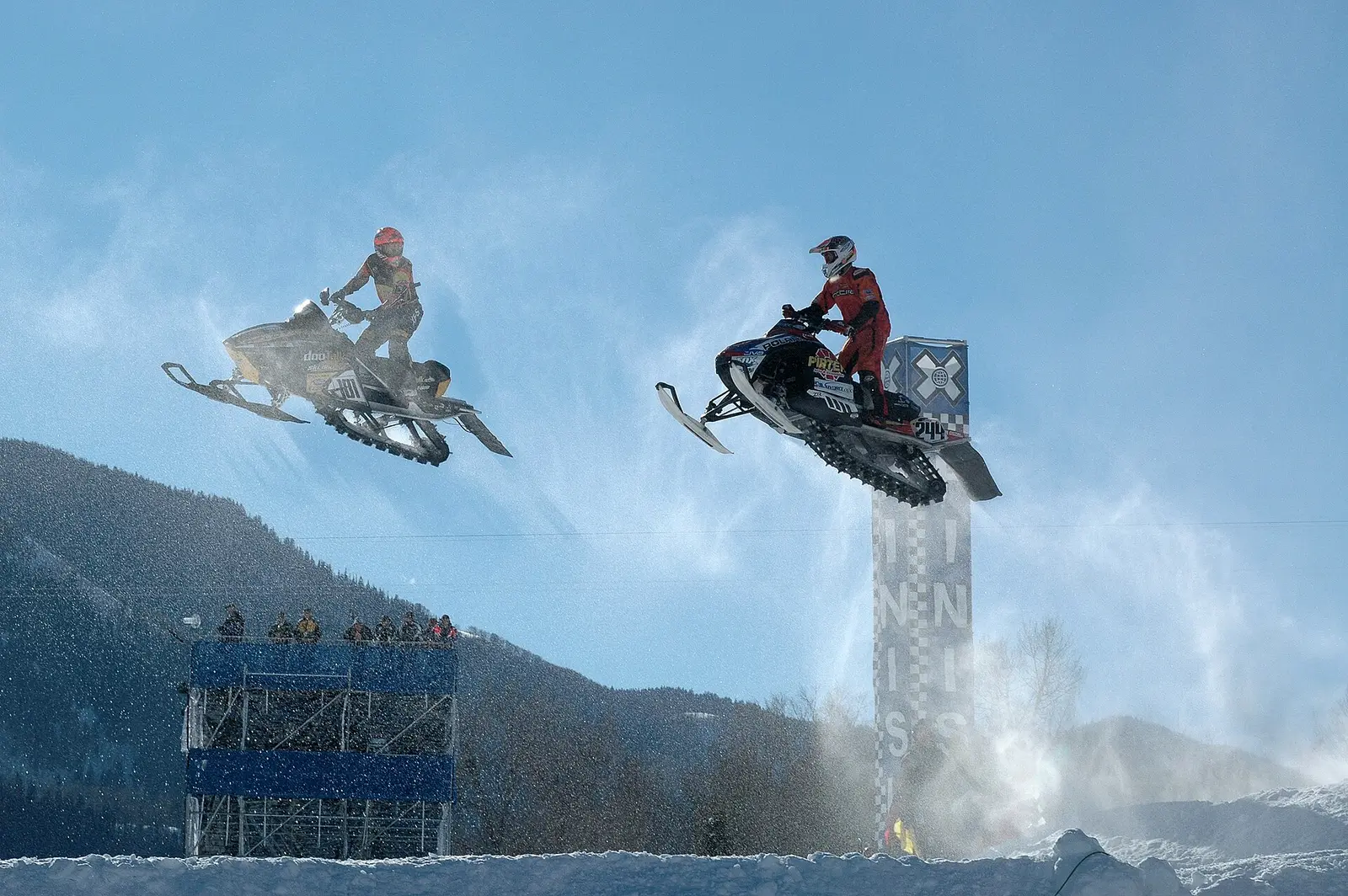 Two snowmobiles in mid-air above the course at an X Games snocross event in Colorado
